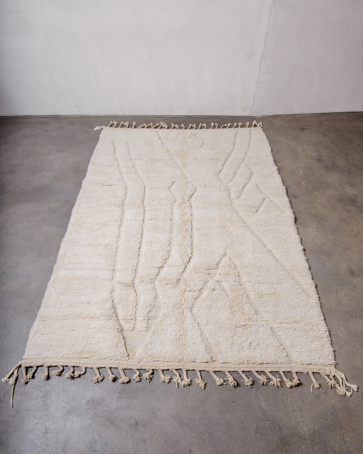 Cream wool rug with design woven in natural wool laying flat on concrete floor.